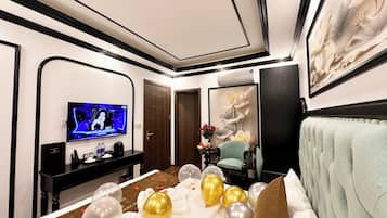 A hotel room with a bed, a TV, a desk, and a large floral painting.