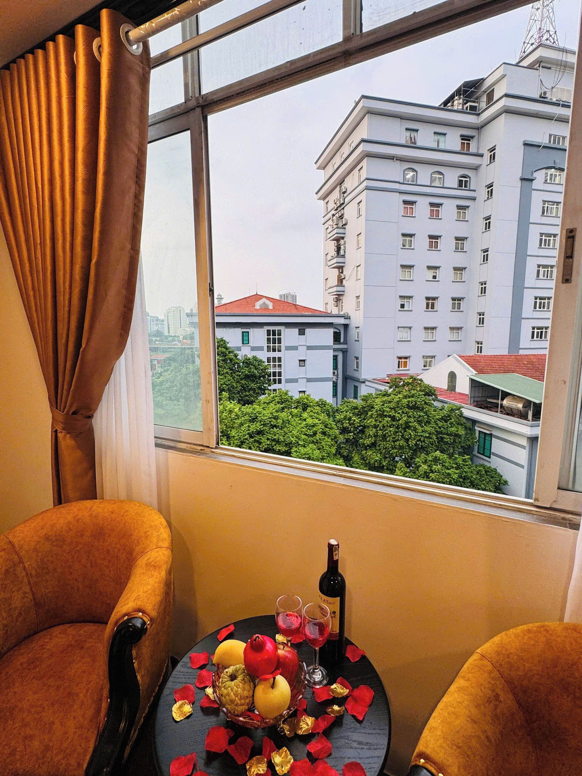 Una habitación con vistas a un edificio, una mesa con una botella y vasos, y dos sillas.