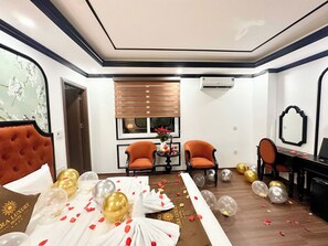 Una habitació d'hotel amb un llit, dues butaques, una taula amb un vas de flors i globus a terra.
