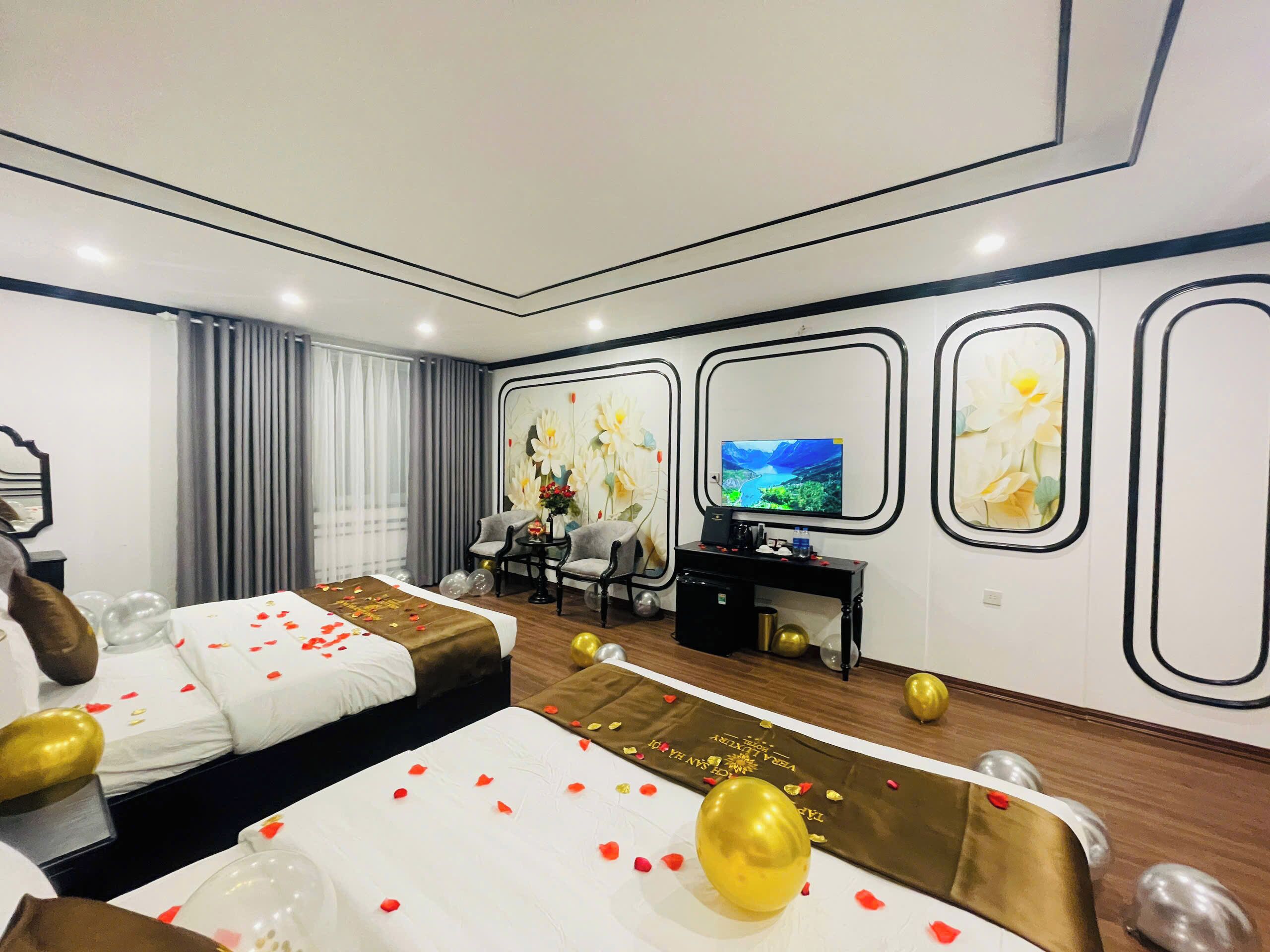 A hotel room with two beds, a television, a desk, and a decorative wall with framed artwork.