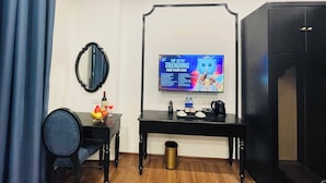 A room with a television displaying a chart, a table with a bottle and glasses, a chair, and a wardrobe. - Vera Luxury Hotel (Hanoi)