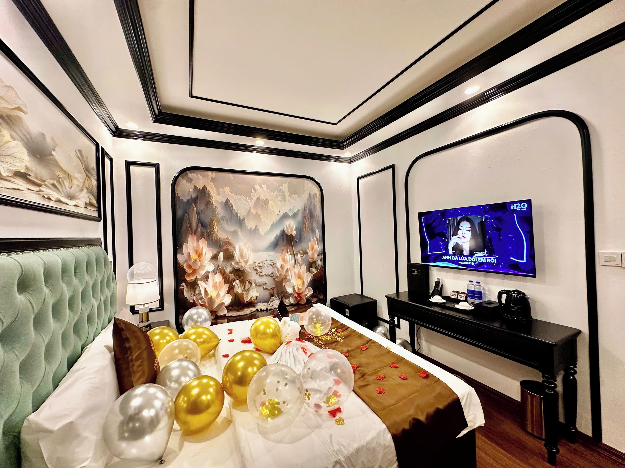 A hotel room with a large bed, a television, and a wall-mounted screen displaying a program.