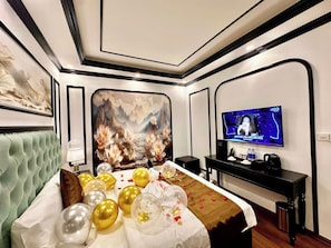 Habitación de hotel con una cama grande, un televisor y una pantalla en la pared mostrando un programa.