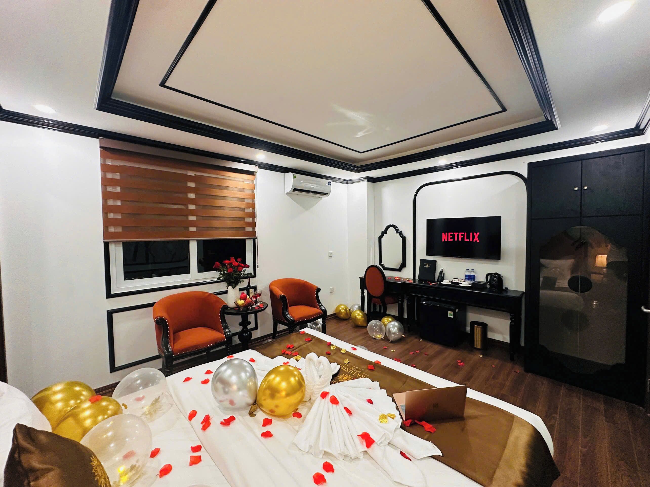 Una habitación de hotel con una cama, dos sillones, un escritorio con una computadora portátil, un televisor y un armario.
