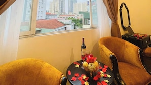A hotel room with a large window, two armchairs, a small table with a bottle and glasses, and a mirror on the wall. - Vera Luxury Hotel (Hanoi)