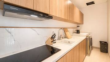 A modern kitchen with wooden cabinets, a black stovetop, a sink, and a dishwasher.