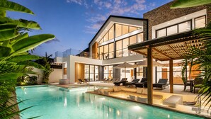 Une maison moderne à deux étages, dotée d’une piscine, d’un espace salon extérieur et d’une façade en pierre.