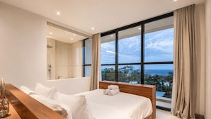 Une chambre moderne avec un grand lit, une table de chevet en bois, une douche intégrée et une vue sur l’océan.