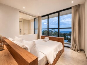 Ein modernes Schlafzimmer mit einem großen Bett, einem Nachttisch aus Holz, einer integrierten Dusche und Meerblick.