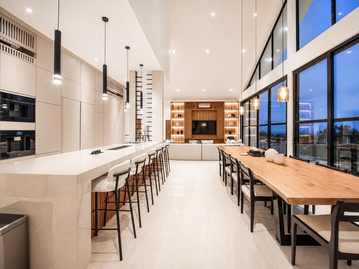 Une cuisine moderne dotée d’un îlot central, de tabourets de bar et d’un coin repas avec une longue table et des chaises en bois.