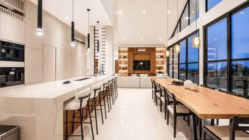 Une cuisine moderne dotée d’un îlot central, de tabourets de bar et d’un coin repas avec une longue table et des chaises en bois.