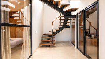 A modern interior with a glass door leading to a bedroom, a staircase with wooden steps and metal railings, and a tiled floor.