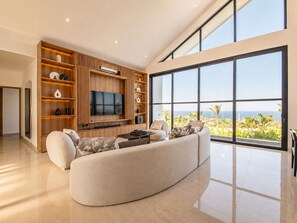 A modern living room with a large window, a flat-screen TV, and a curved sofa.
