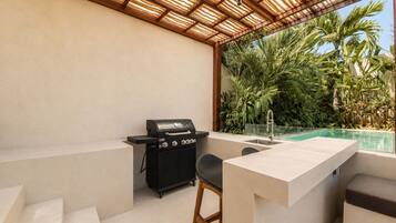 Une terrasse extérieure équipée d’un barbecue, d’une piscine et d’un espace salon.