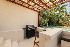 An outdoor patio with a grill, a pool, and a seating area.
