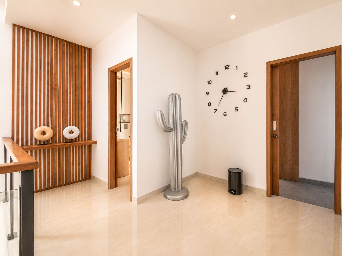 Un interior moderno con un revestimiento de listones de madera, una escultura de cactus, un reloj de pared y un cubo de basura.
