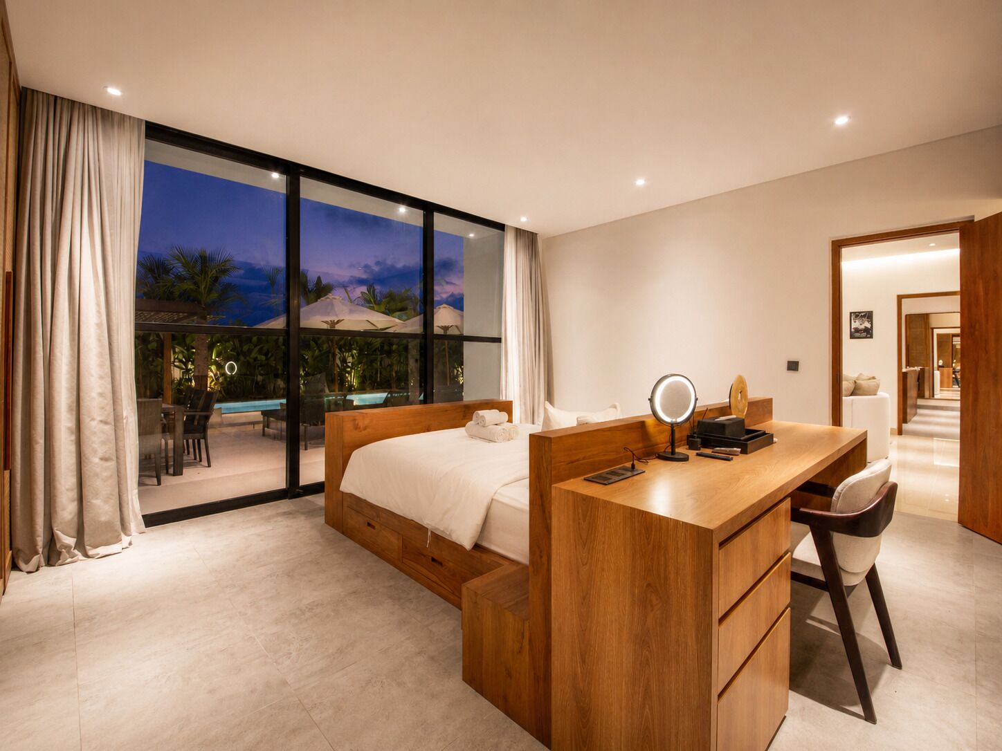 A modern hotel room with a large bed, a wooden desk, and a view of a pool area.