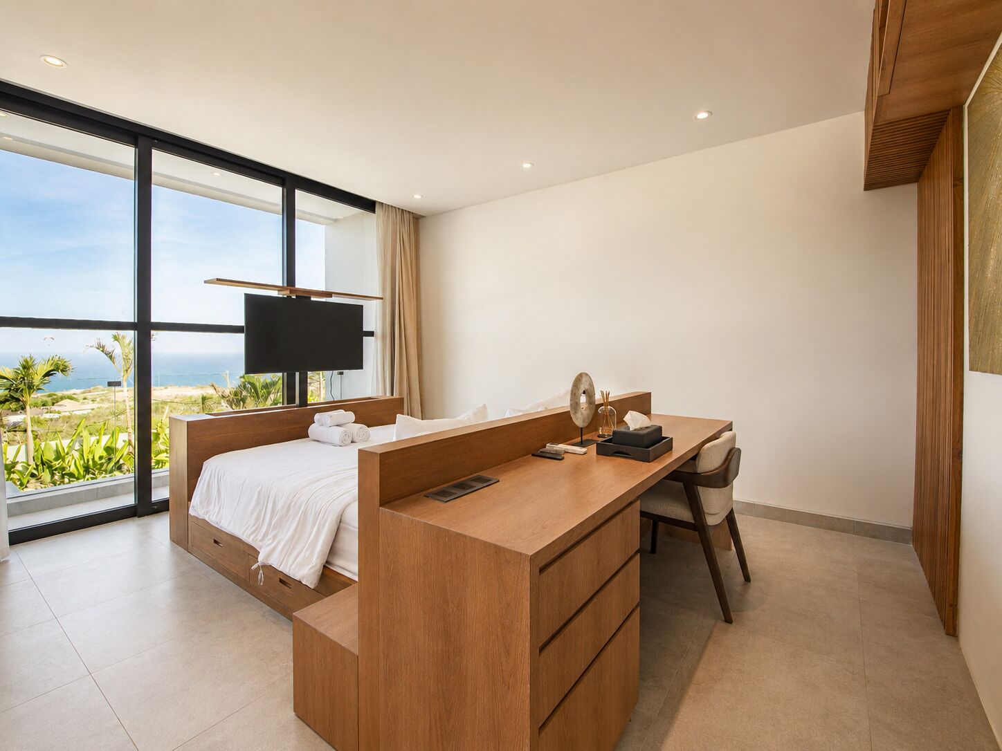 Une chambre d’hôtel moderne dotée d’un grand lit, d’un bureau avec une chaise, d’une télévision et offrant une vue sur l’océan.