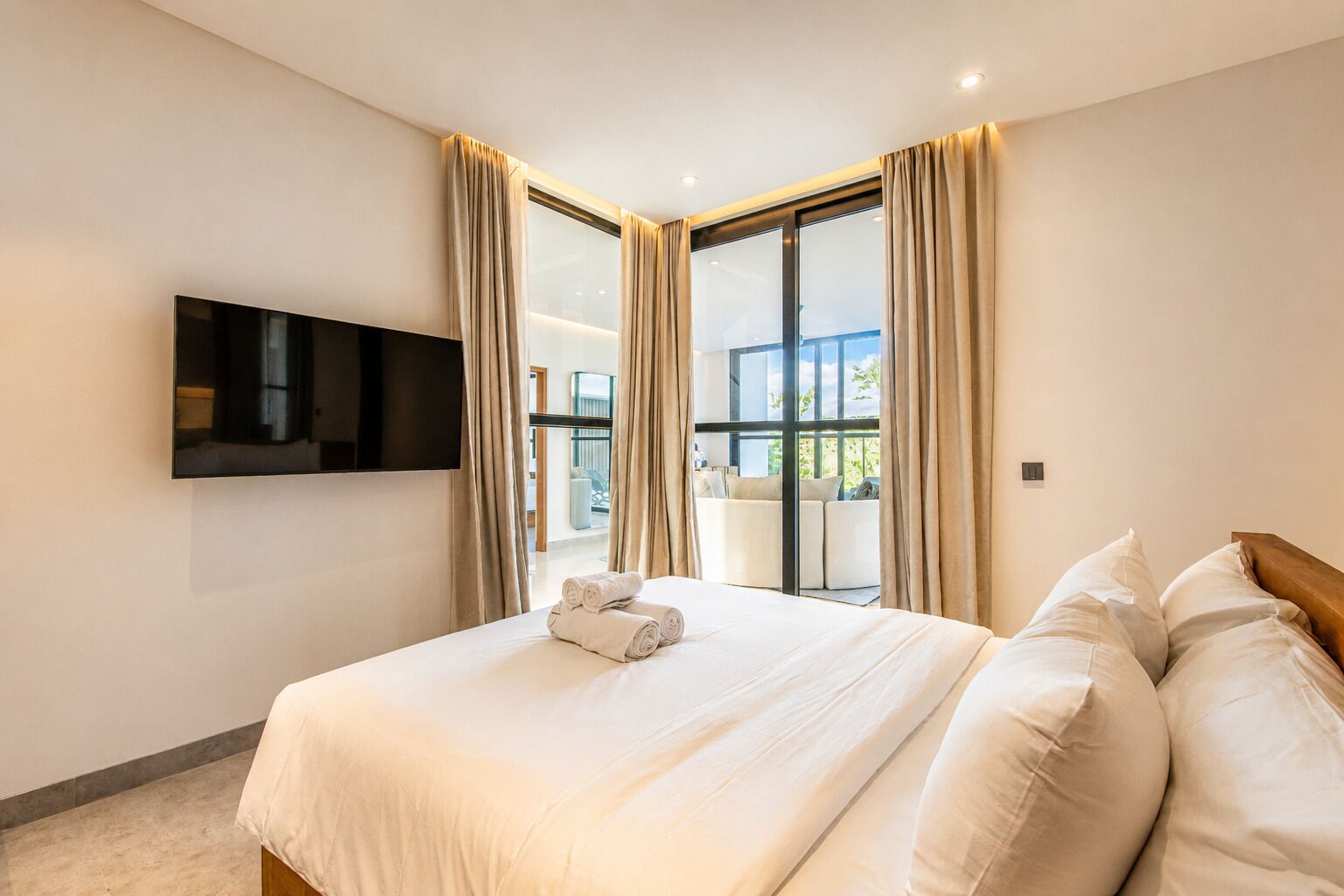 A hotel room with a bed, a flat-screen TV, and a balcony with curtains.