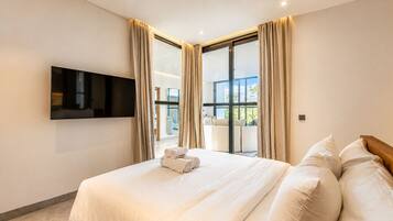 A hotel room with a bed, a flat-screen TV, and a balcony with curtains.