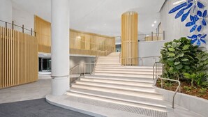 Ein modernes Interieur mit einer zentralen Treppe, Holzlamellen und einer blauen Wand mit Blattmuster.