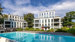 Et moderne hotel med swimmingpool, flere balkoner og en velholdt have.