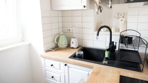A kitchen with white cabinets, a black sink, a green kettle, and a black coffee maker. - Studio apartment Milica  (Kaštel Novi)