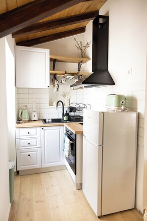 Cocina compacta con armarios blancos, encimera de madera, campana extractora negra y un refrigerador pequeño.