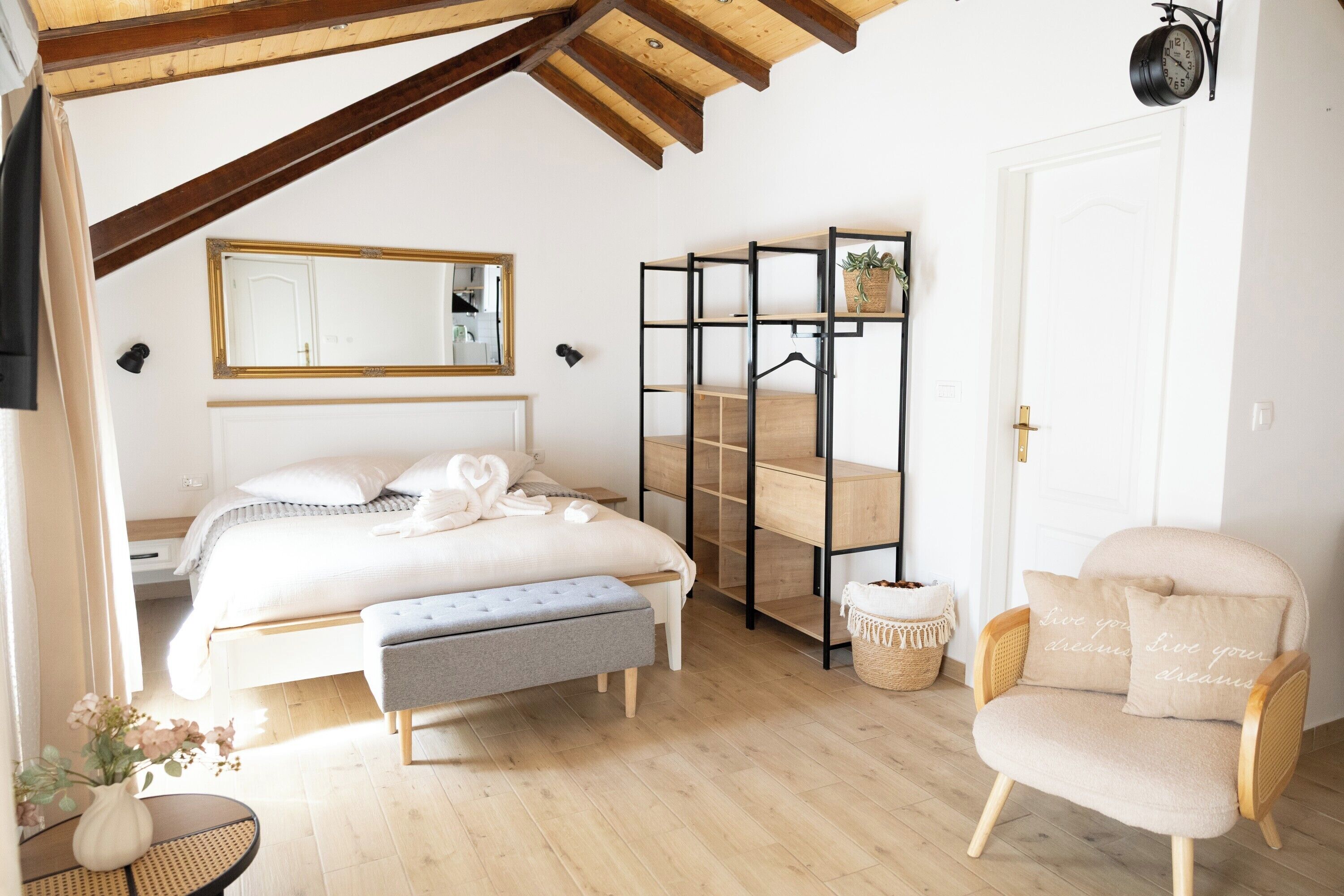 A bedroom with a bed, bench, chair, bedside table, mirror, and a wall-mounted shelf with a plant.