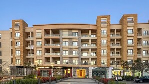 Ein mehrstöckiges Hotel mit Balkonen, einem zentralen Eingangsbereich und einem Parkplatz.