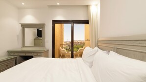 Ein Hotelzimmer mit Bett, Schminktisch, Spiegel, einem Balkon mit Stühlen und Blick auf Gebäude.