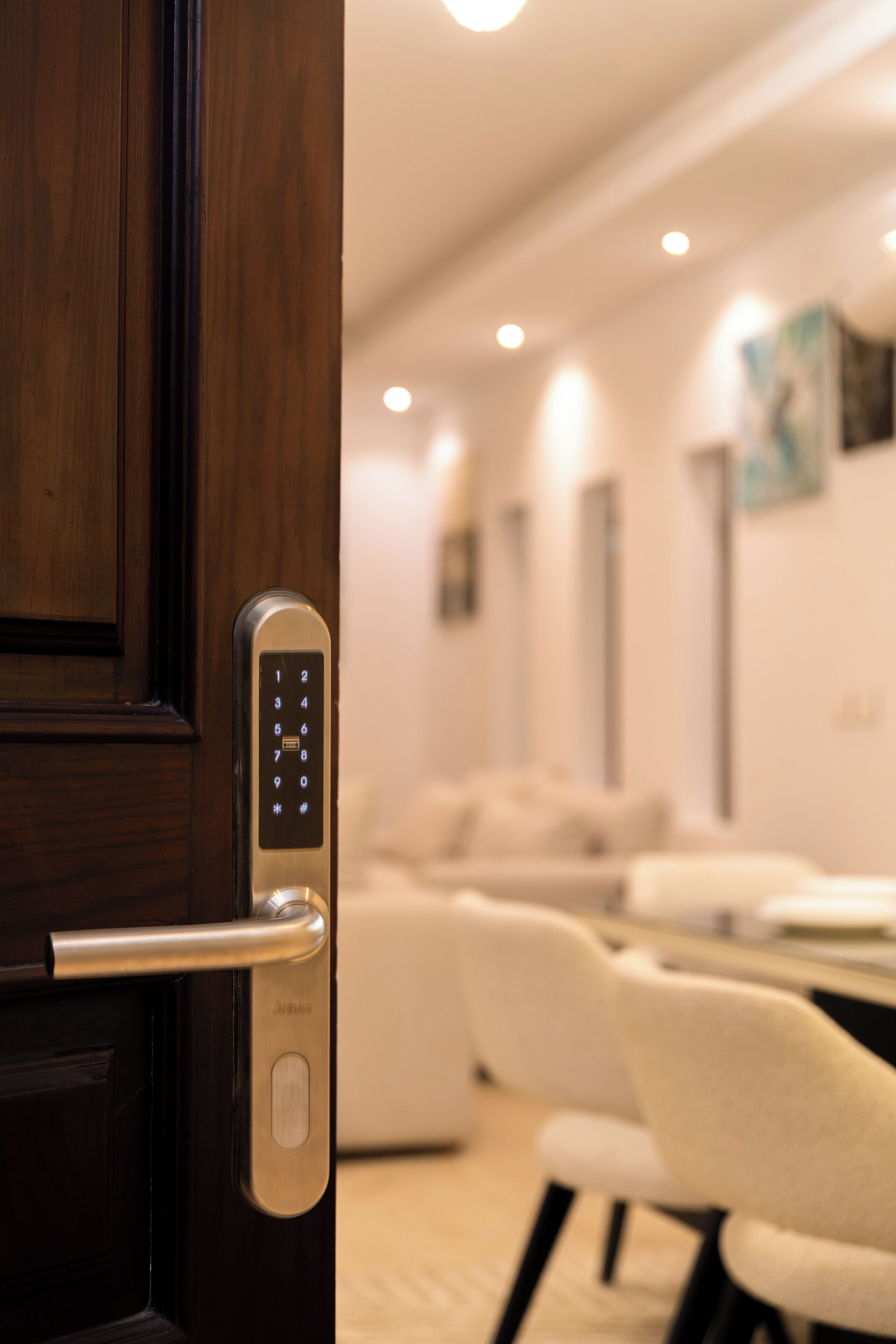 A modern hotel room with a wooden door, a digital keypad lock, a white sofa, and a dining table.