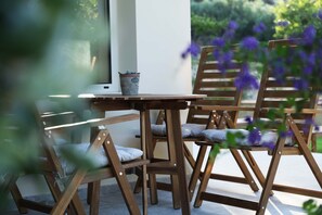 Une table et des chaises en bois, agrémentées de coussins, une plante en pot et une vue sur la verdure.
