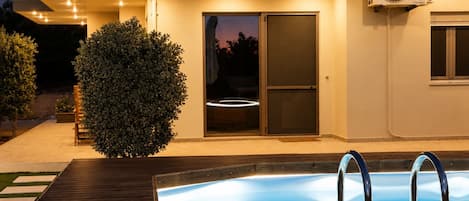 A modern house with a swimming pool, a covered patio, and a large fan mounted on the exterior wall.