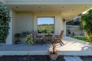 Une terrasse couverte avec une table et des chaises, des plantes en pot et une vue sur une colline.