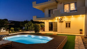 A modern two-story house with a swimming pool, outdoor furniture, and a well-lit balcony. - Olive Raki Luxury Pool Villa Crete Garden Oasis (Malevizi)