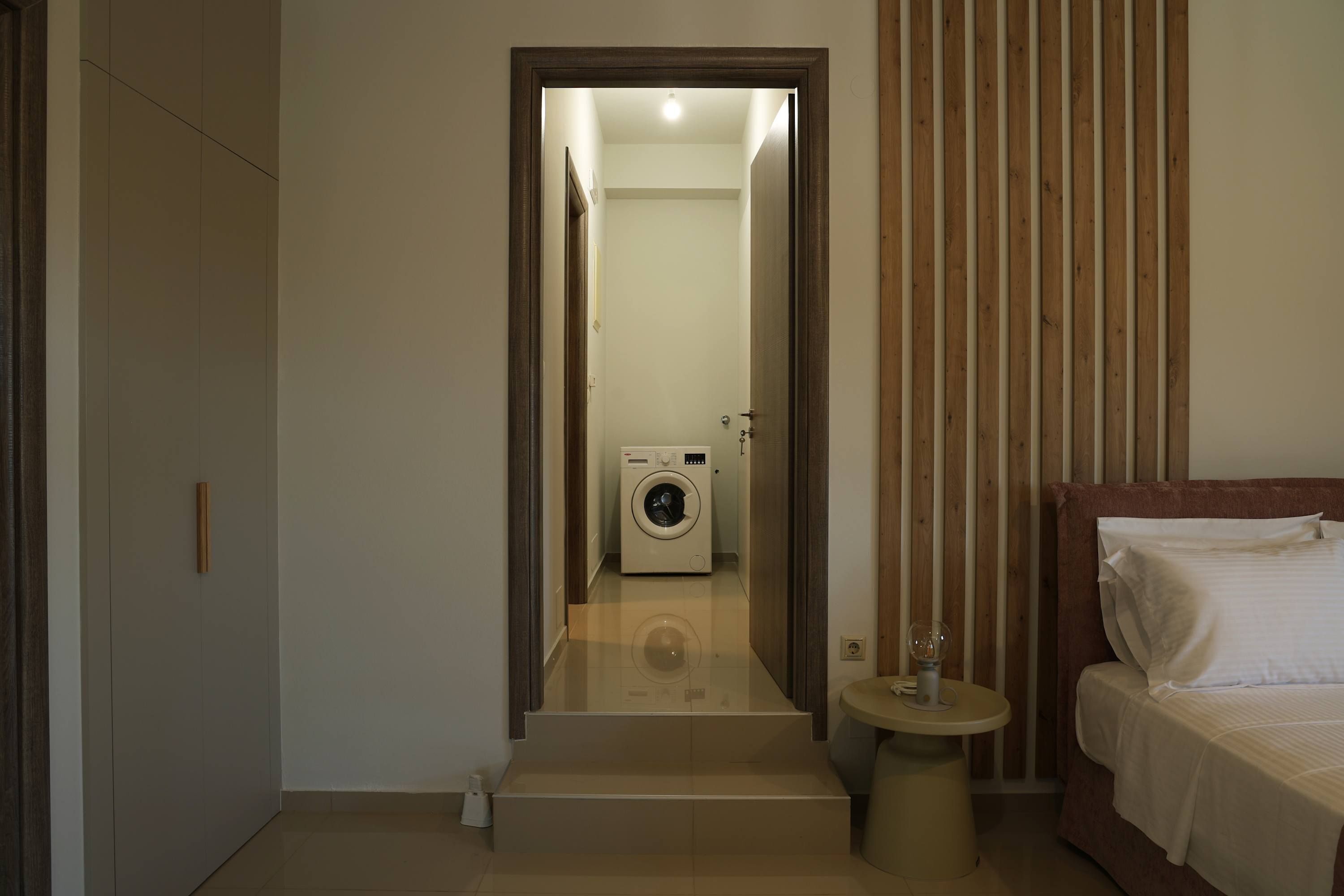 A hotel room with a bed, a washing machine, a small table, and a door leading to another room.
