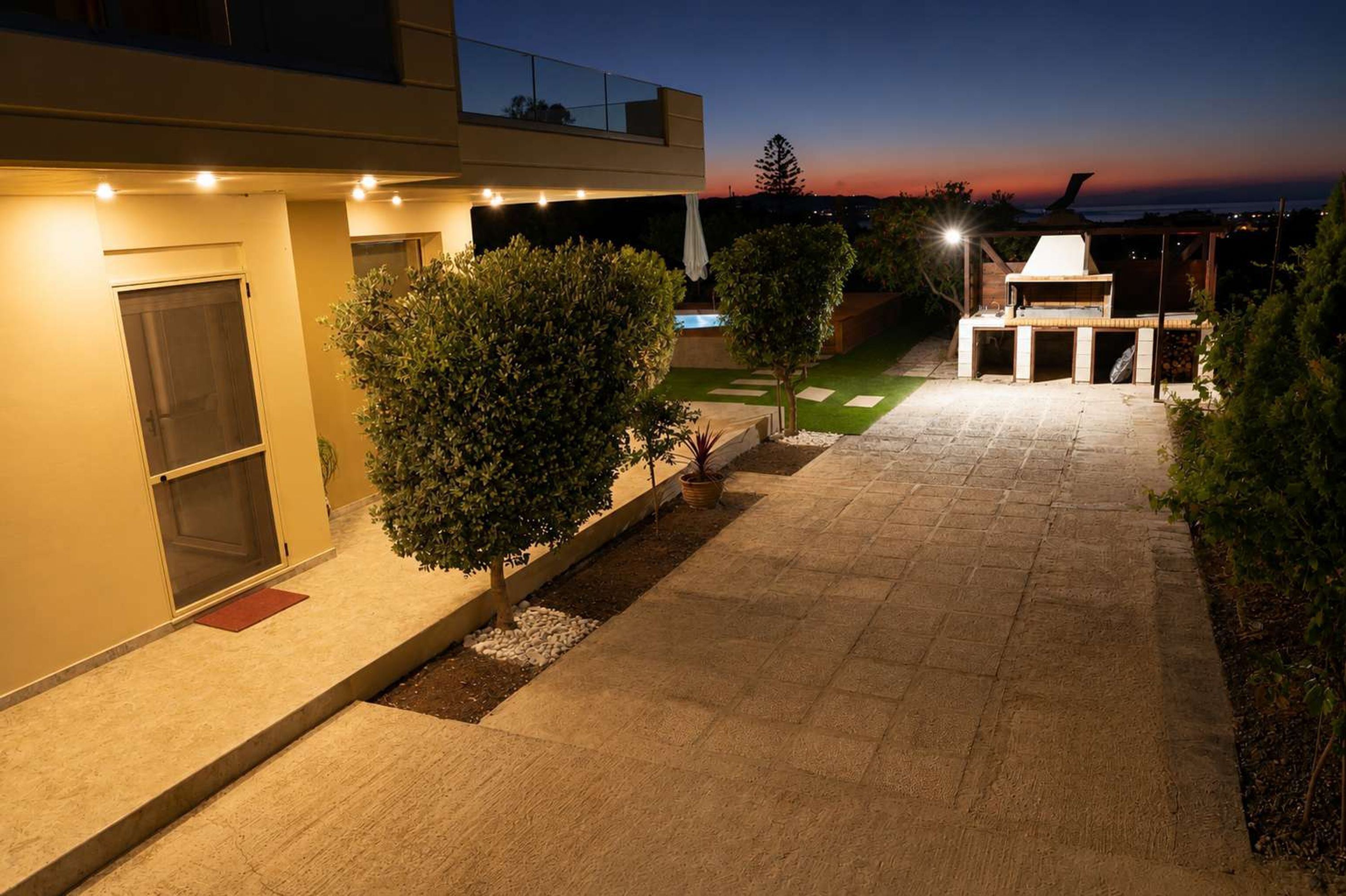A modern outdoor patio area with a barbecue, a small pool, and a well-lit pathway.