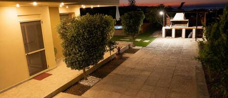 A modern outdoor patio area with a barbecue, a small pool, and a well-lit pathway.