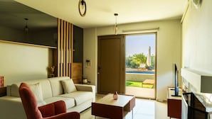 A modern living room with a sofa, a coffee table, a red chair, a fireplace, and a sliding glass door leading to an outdoor area. - Olive Raki Luxury Pool Villa Crete Garden Oasis (Malevizi)