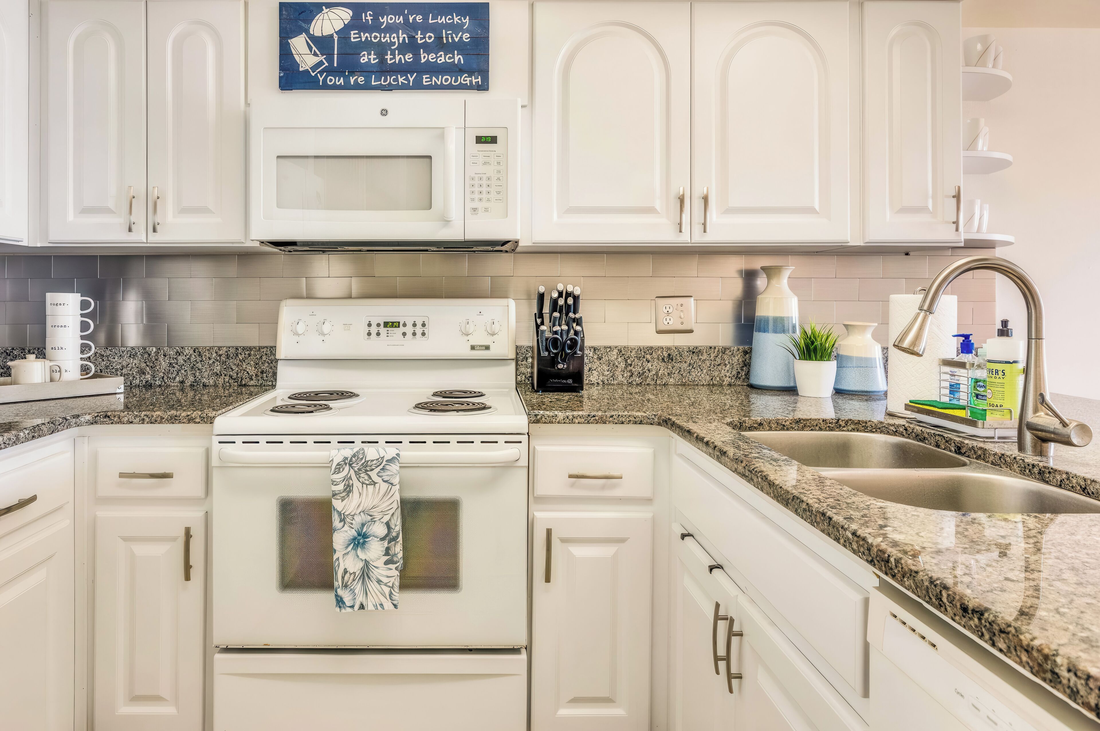 A kitchen with white cabinets, a microwave, stove, and a sink with granite countertops.