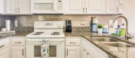 A kitchen with white cabinets, a microwave, stove, and a sink with granite countertops.