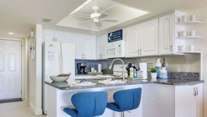 A modern kitchen with white cabinets, a central island with bar stools, a ceiling fan, and a sign on the wall.