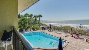 A pool with a view of the beach, lounge chairs, and umbrellas.