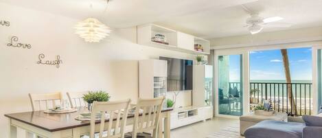 A dining area with a table and chairs, a TV, and a balcony with a view.