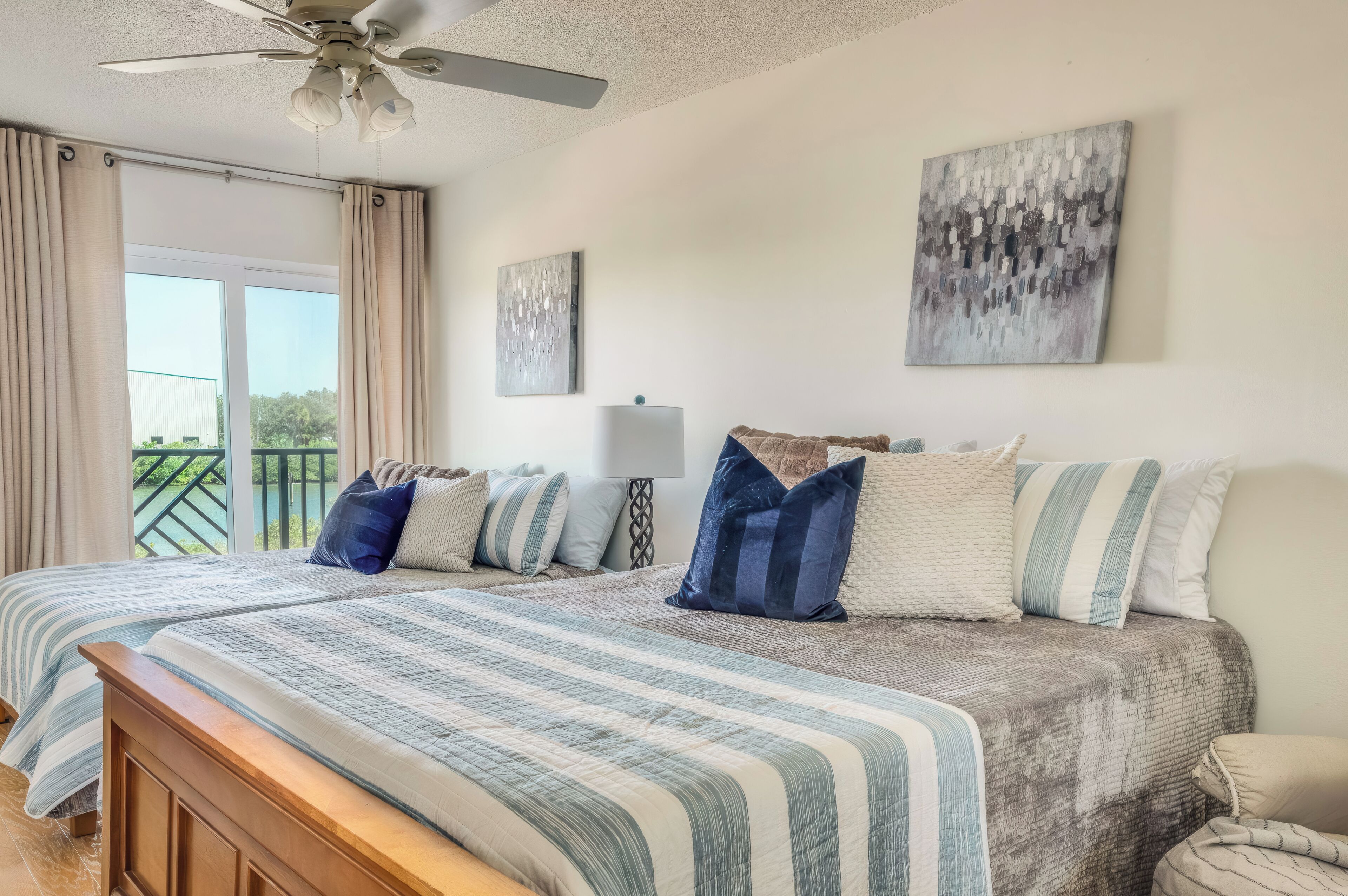 A bedroom with two beds, a ceiling fan, and artwork on the walls.