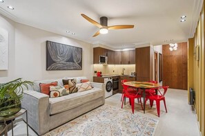 Ein modernes Wohnzimmer mit einer Couch, roten Sesseln, einem Esstisch und einem Deckenventilator.