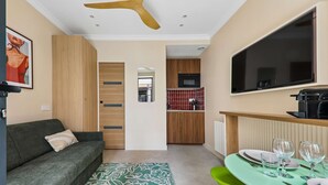 A compact living space with a sofa, a dining table set for four, a kitchen area, and a television mounted on the wall. - Charming Studio 2P Near Marais-bastille (Paris)