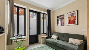 A room with a green sofa, a small table, a green chair, a patterned rug, and two framed pictures on the wall. - Charming Studio 2P Near Marais-bastille (Paris)