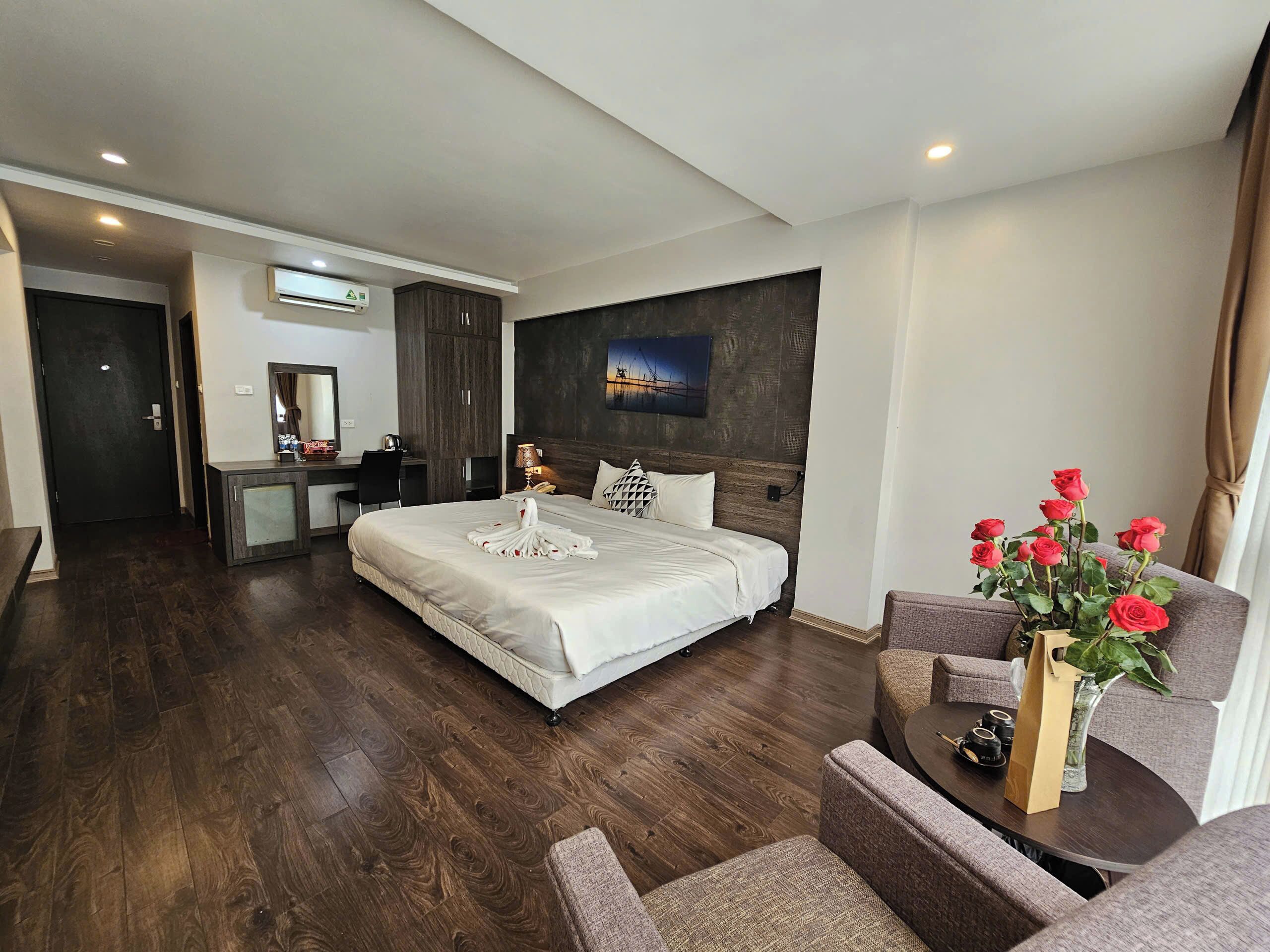 A hotel room with a large bed, a desk, a chair, a sofa, and a vase with flowers.
